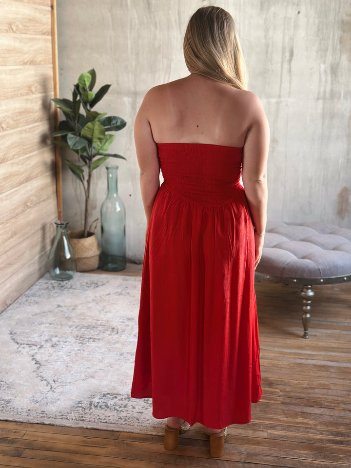 Woman wearing a strapless red dress in a room with a plant and a chair.