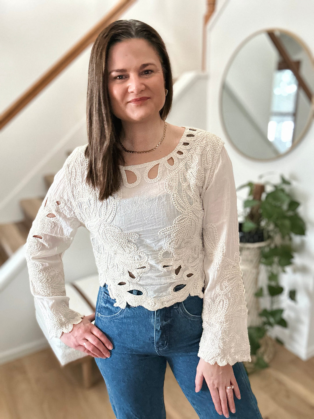 Woman wearing a white lace top and blue jeans indoors.