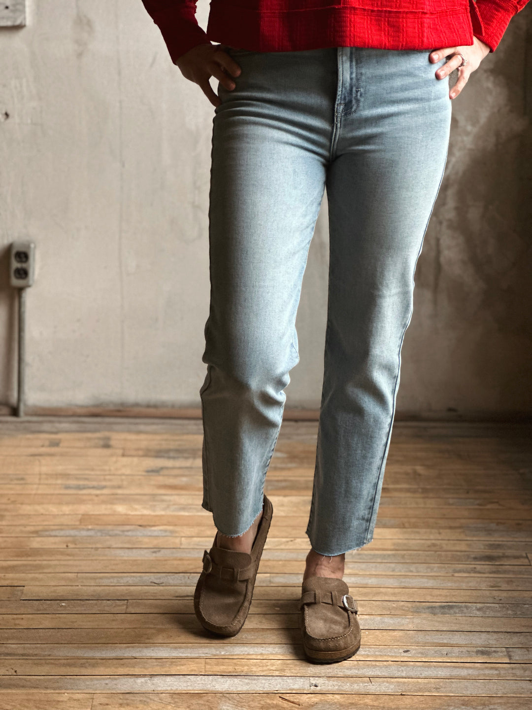 Person wearing light blue jeans and brown shoes standing on a wooden floor.