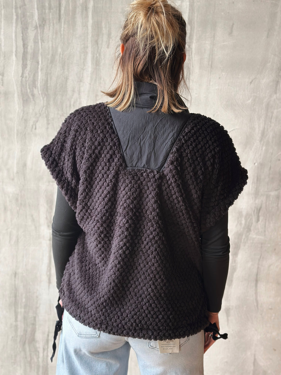 Person wearing a dark brown knitted poncho against a light gray background