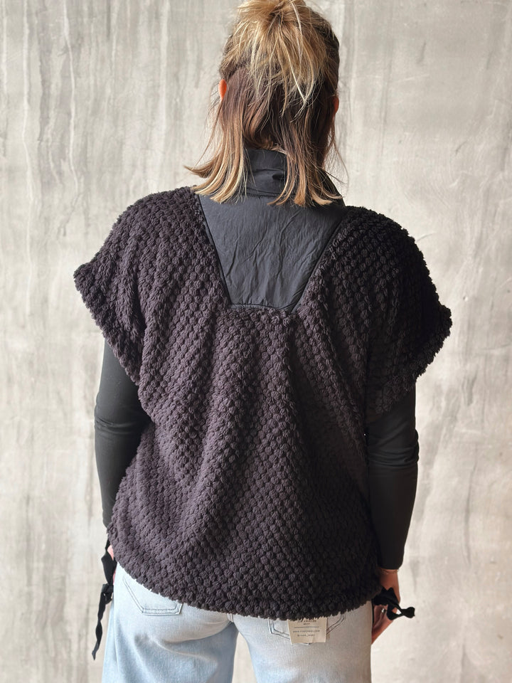 Person wearing a dark brown knitted poncho against a light gray background