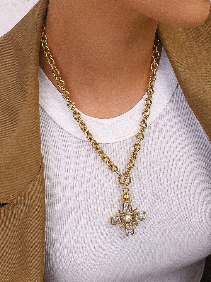 Gold chain necklace with a cross pendant worn by a person in a white shirt and brown jacket.