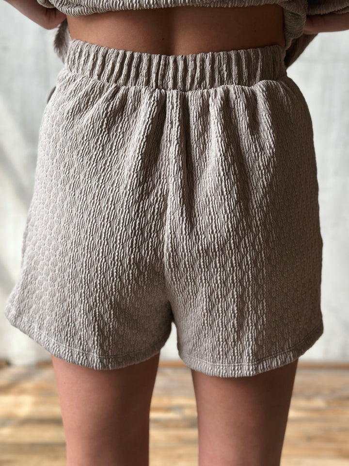 Person wearing textured gray shorts with a neutral background