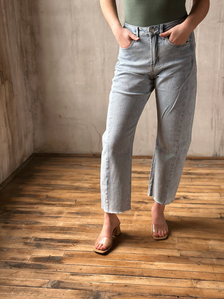 Person wearing light blue jeans standing on a wooden floor with a neutral wall background
