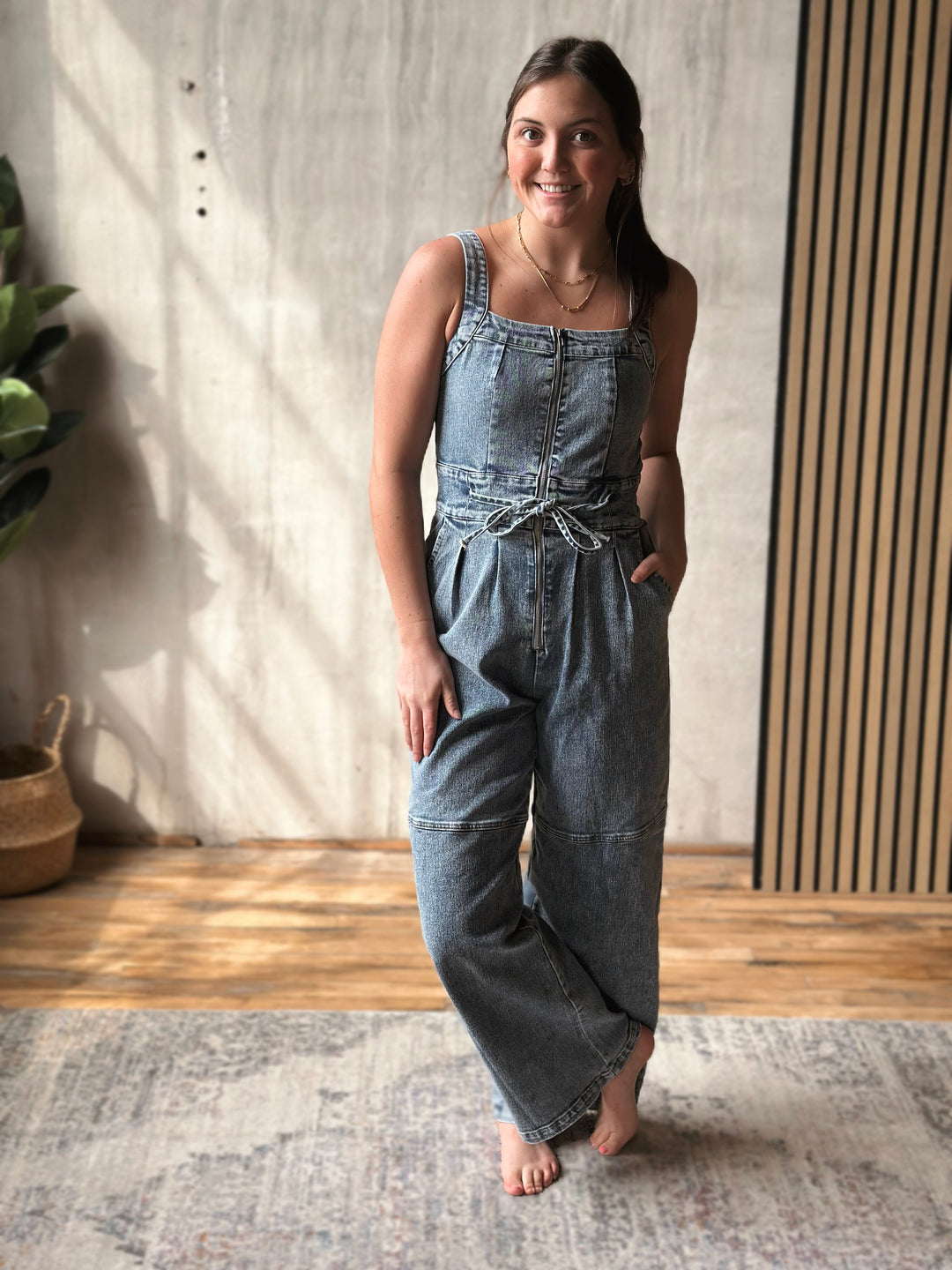 Woman wearing a denim jumpsuit standing indoors with a neutral background