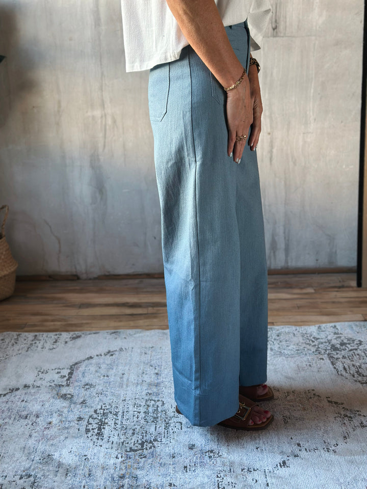 Person wearing light blue wide-leg pants and a white shirt in a room with a textured wall and rug.