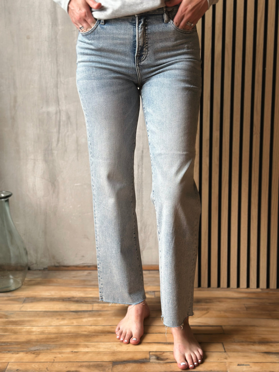 Person wearing light blue jeans standing on a wooden floor with a neutral background
