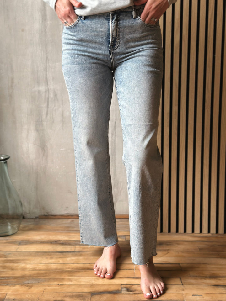Person wearing light blue jeans standing on a wooden floor with a neutral background