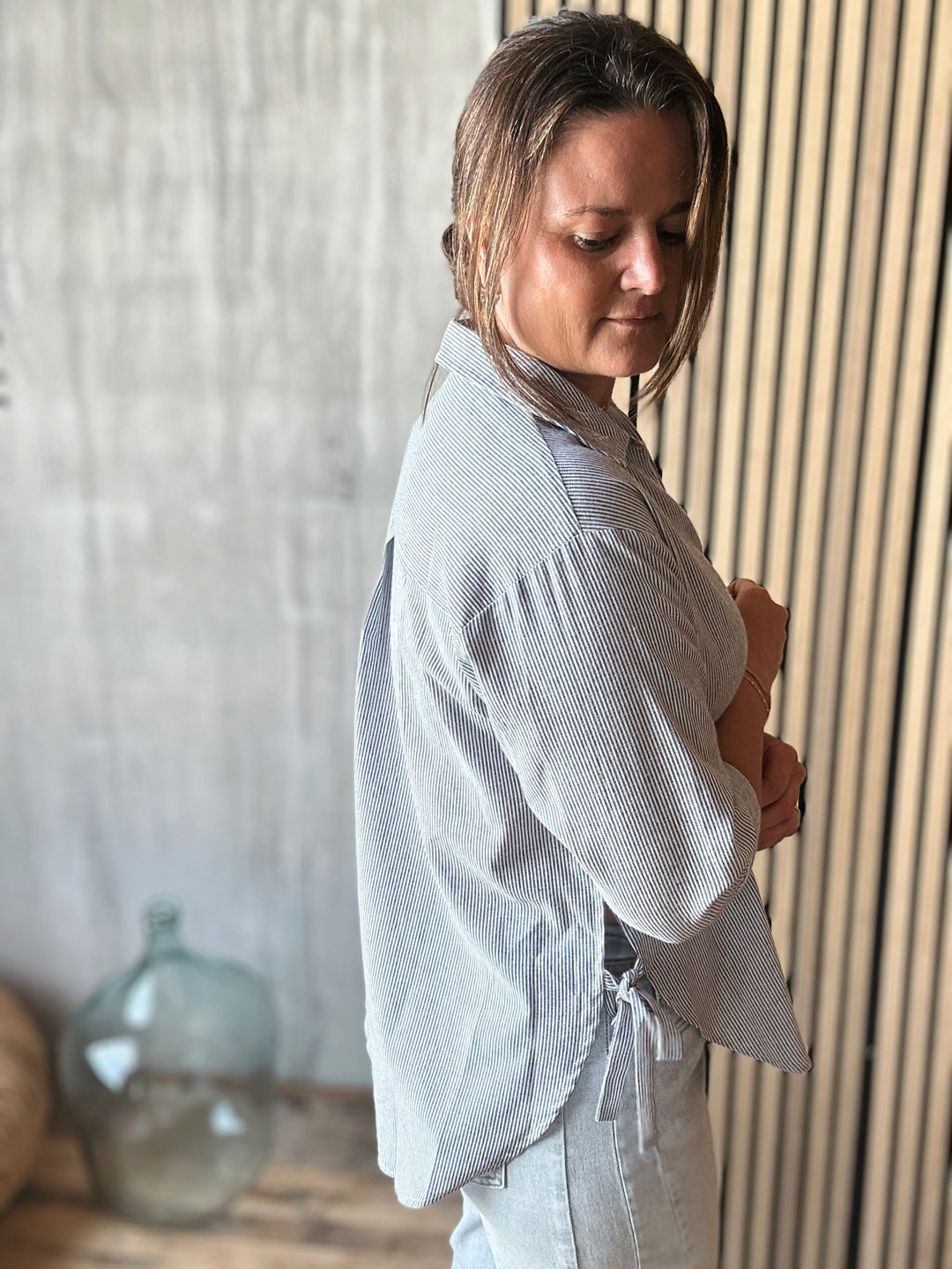 Woman wearing a light blue stripe shirt and pants in a room with wooden paneling.