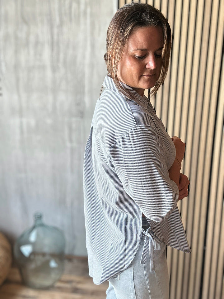 Woman wearing a light blue stripe shirt and pants in a room with wooden paneling.