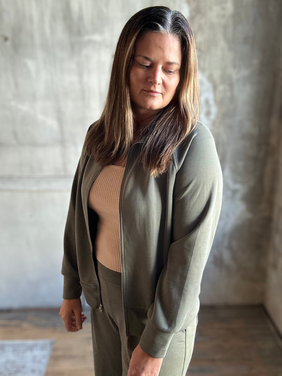 Olive green zip-up sweatshirt worn open over a tan top, angled view