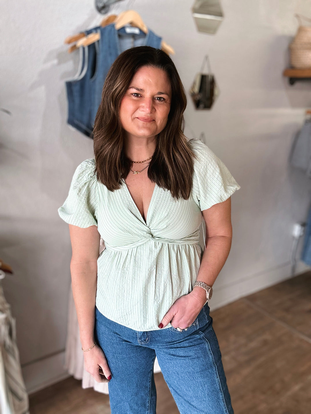 Woman wearing a light green top and blue jeans in a clothing store.