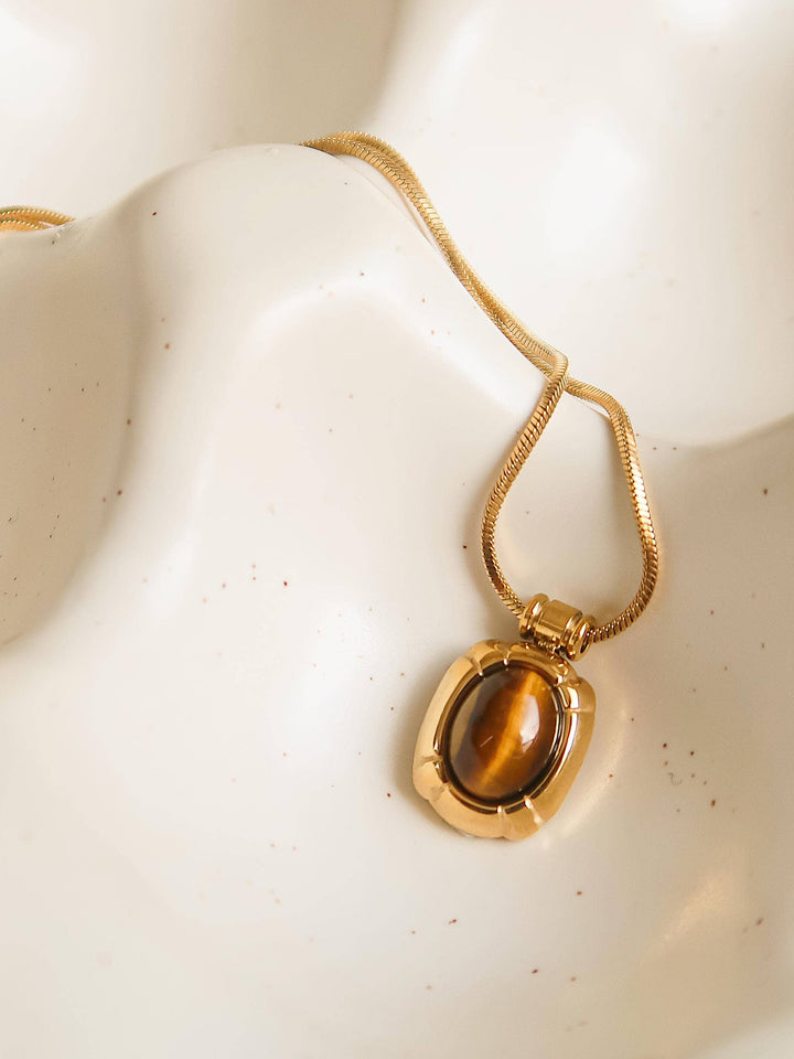 Gold necklace with a tiger's eye pendant on a mannequin bust.
