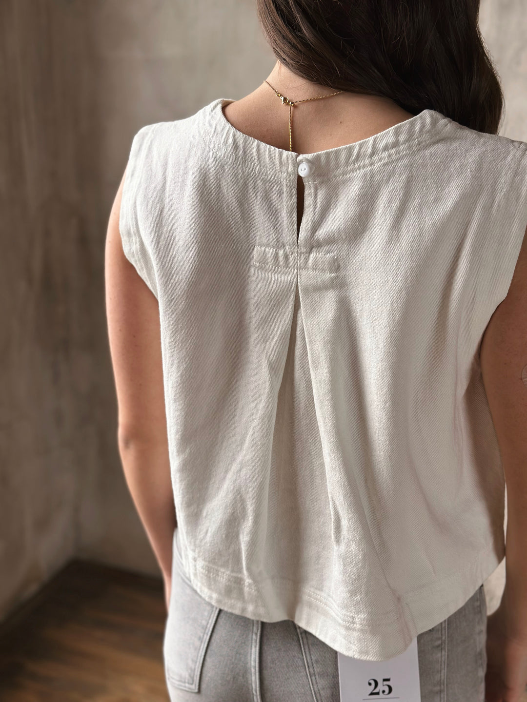 Person wearing a white denim sleeveless top with a neutral background