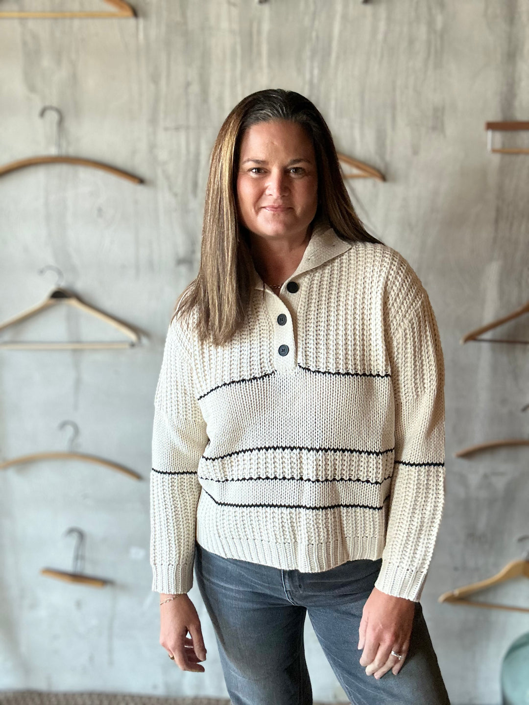 Woman wearing a cream collared sweater with black buttons and wavy stripes