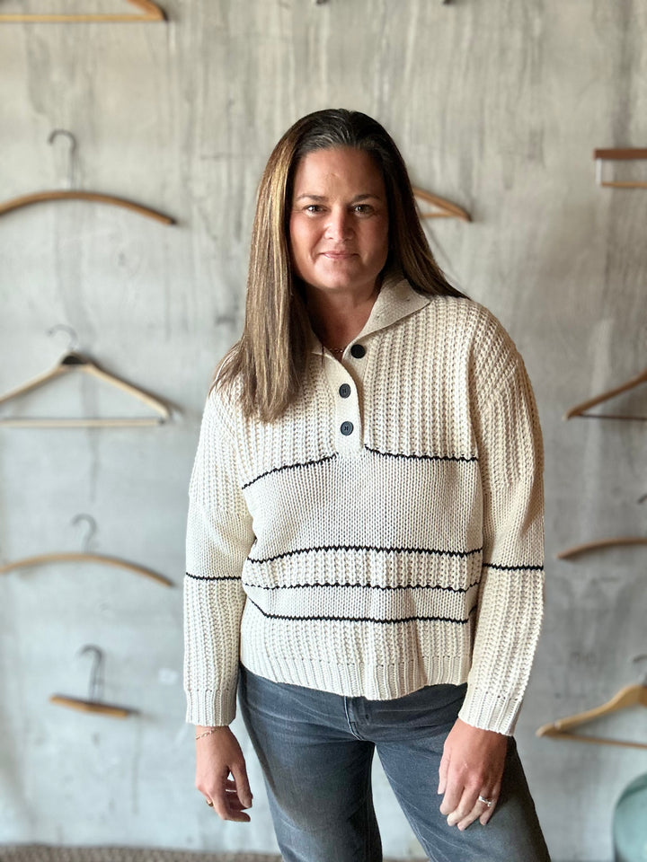 Woman wearing a cream collared sweater with black buttons and wavy stripes