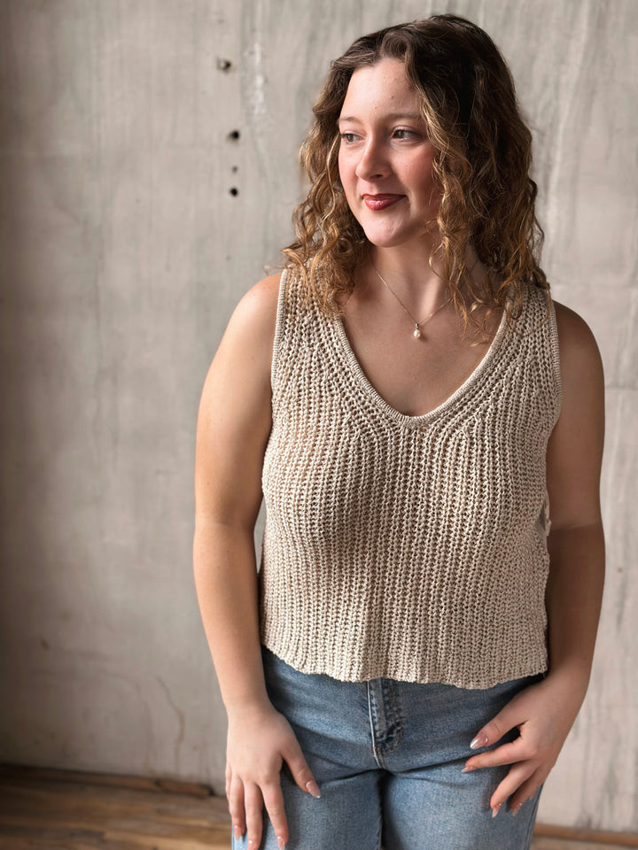 Woman wearing a beige knitted tank top against a neutral background