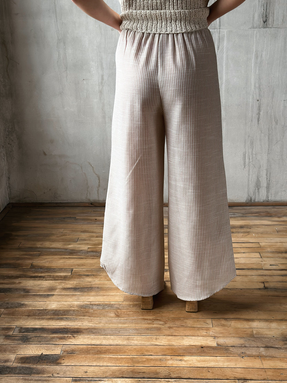 Person wearing beige ribbed pants standing on a wooden floor with a gray wall background
