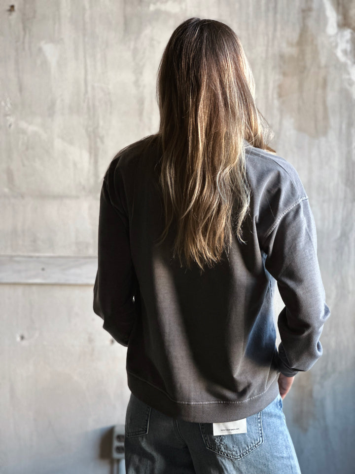 Person wearing a black jacket and blue jeans standing against a textured wall.