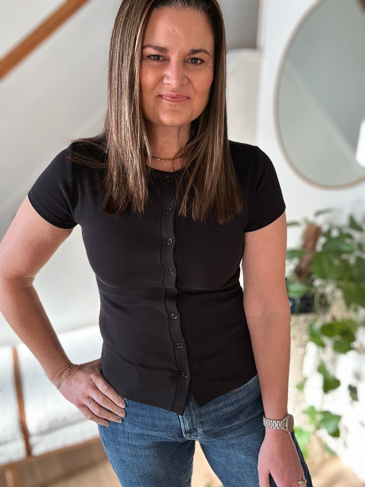 Woman wearing a black shirt and blue jeans indoors with a blurred background