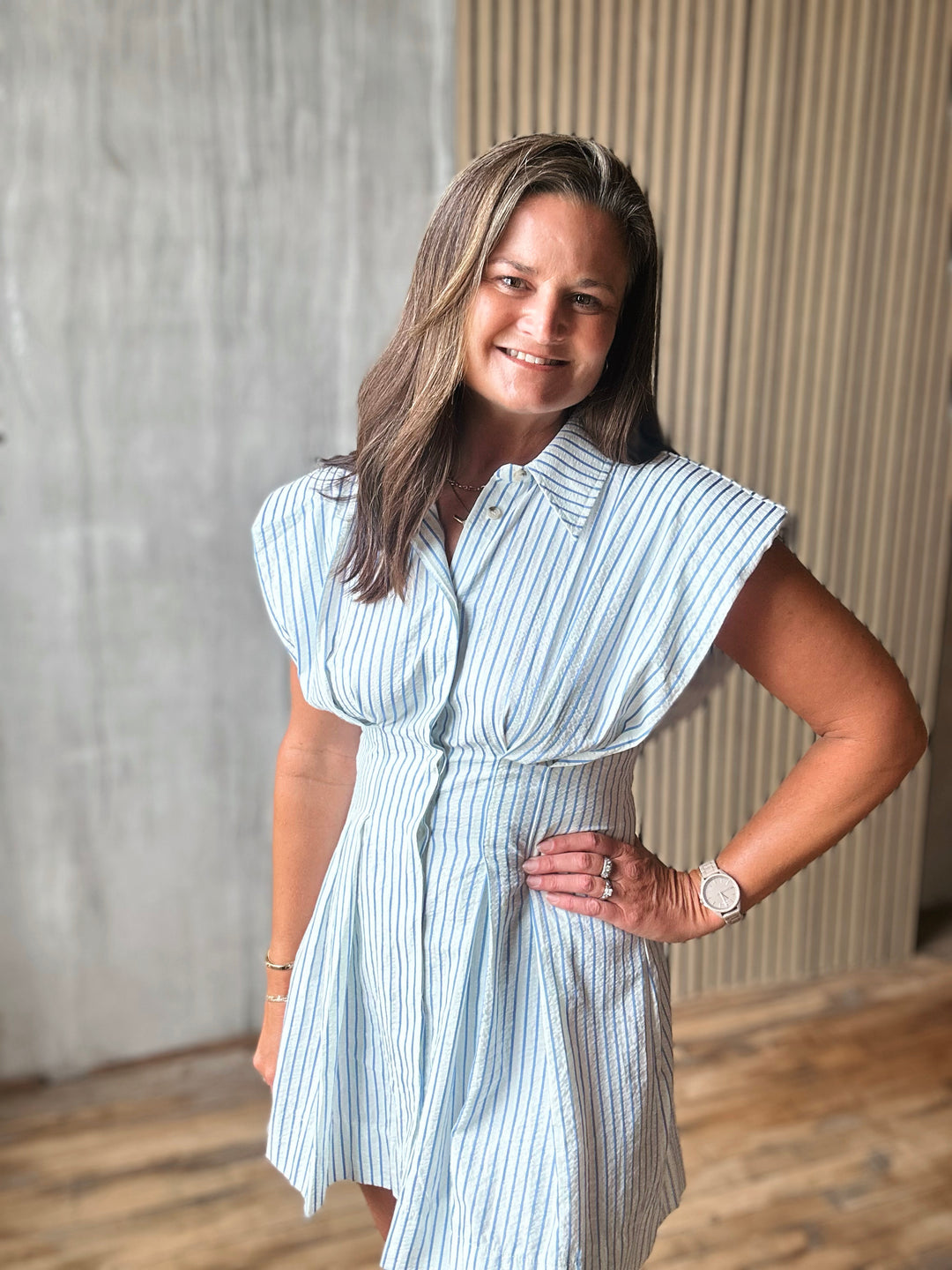 Woman wearing a light blue striped dress standing indoors against a neutral background