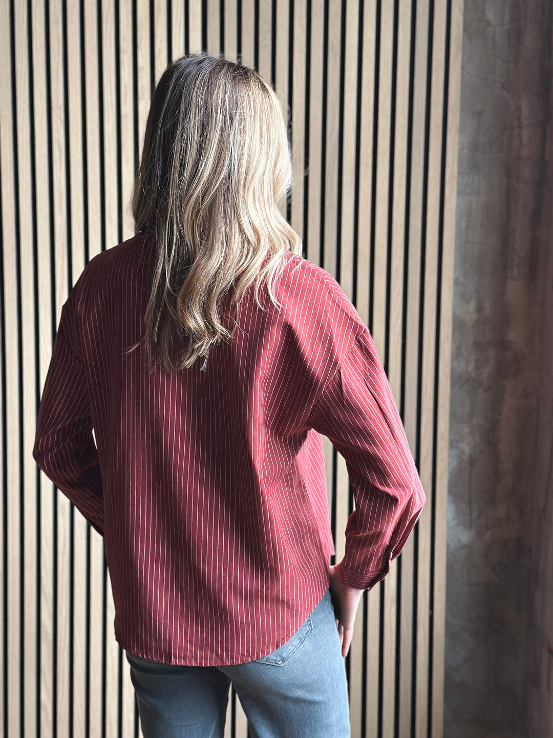 Person wearing a red ribbed sweater standing against a striped wall.