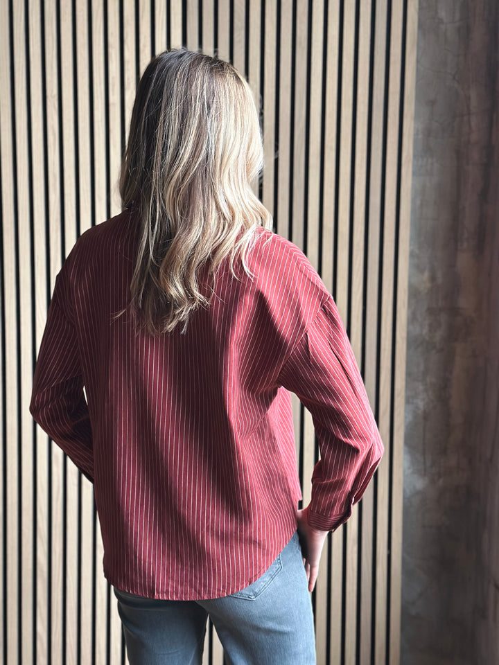 Person wearing a red ribbed sweater standing against a striped wall.