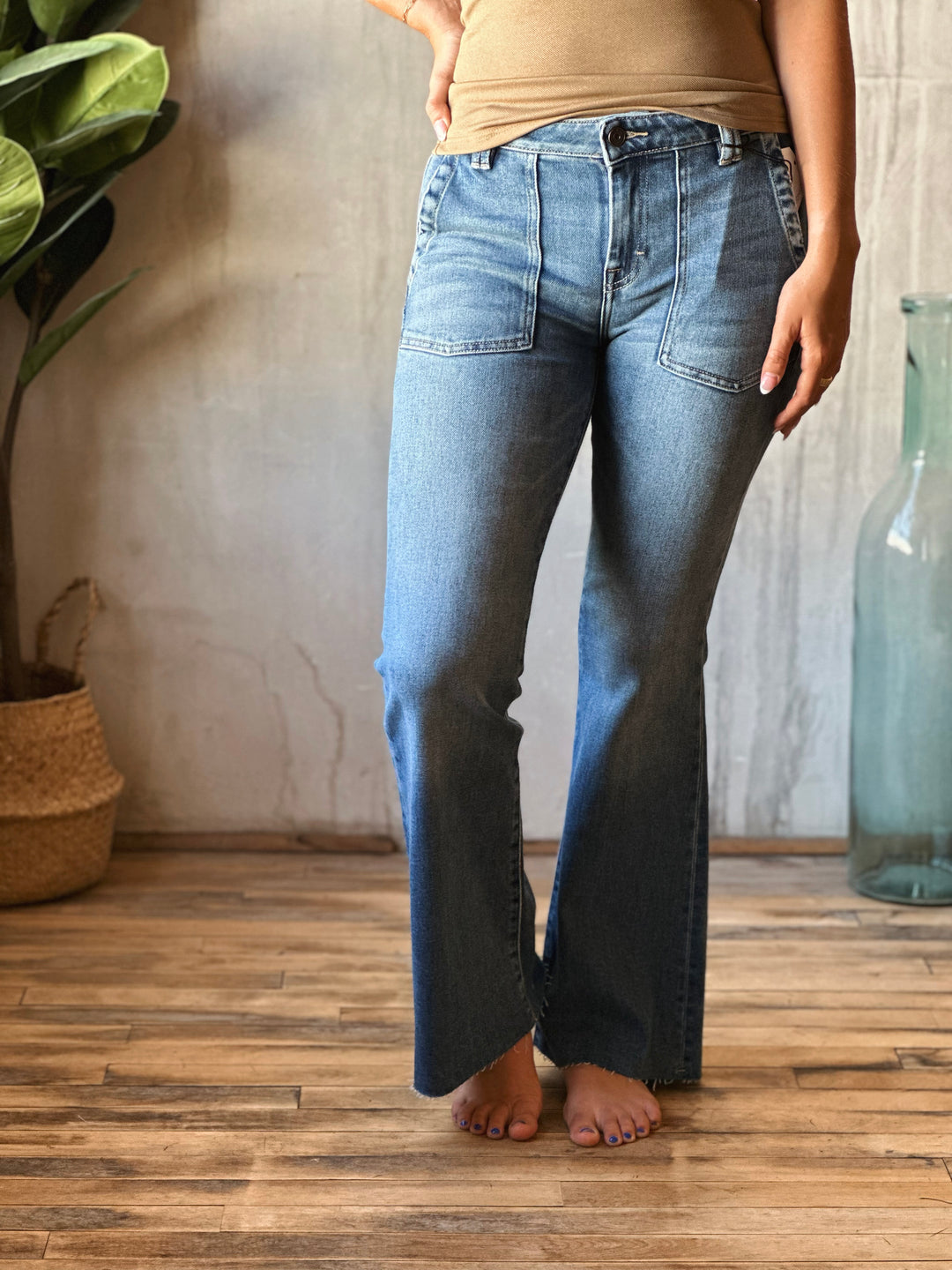 Person wearing blue jeans standing in a room with a plant and vase in the background