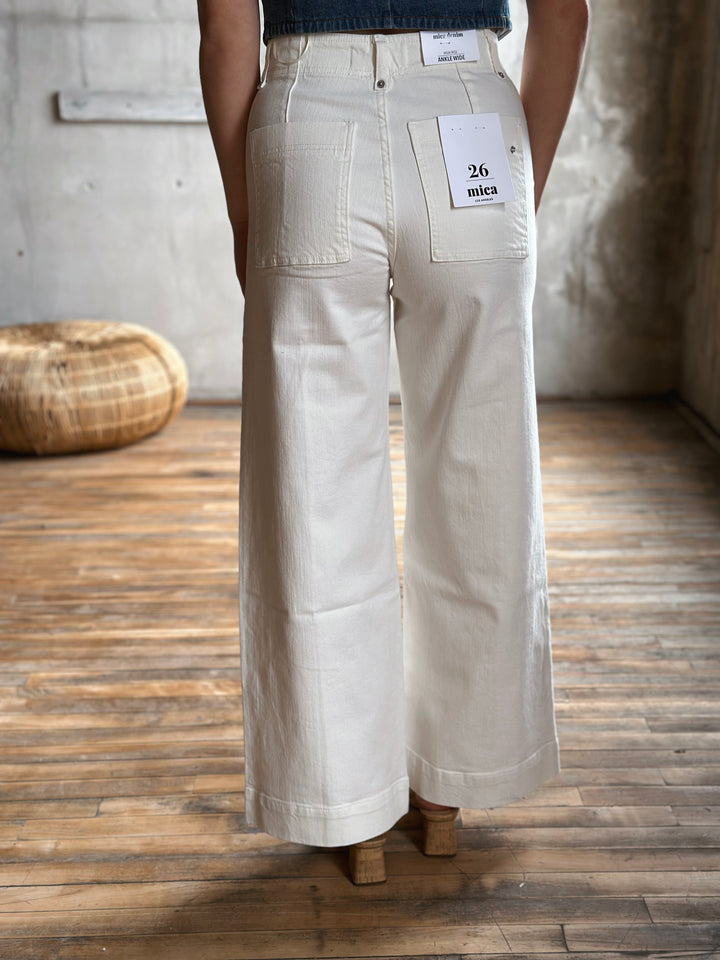 Person wearing white jeans on a wooden floor.