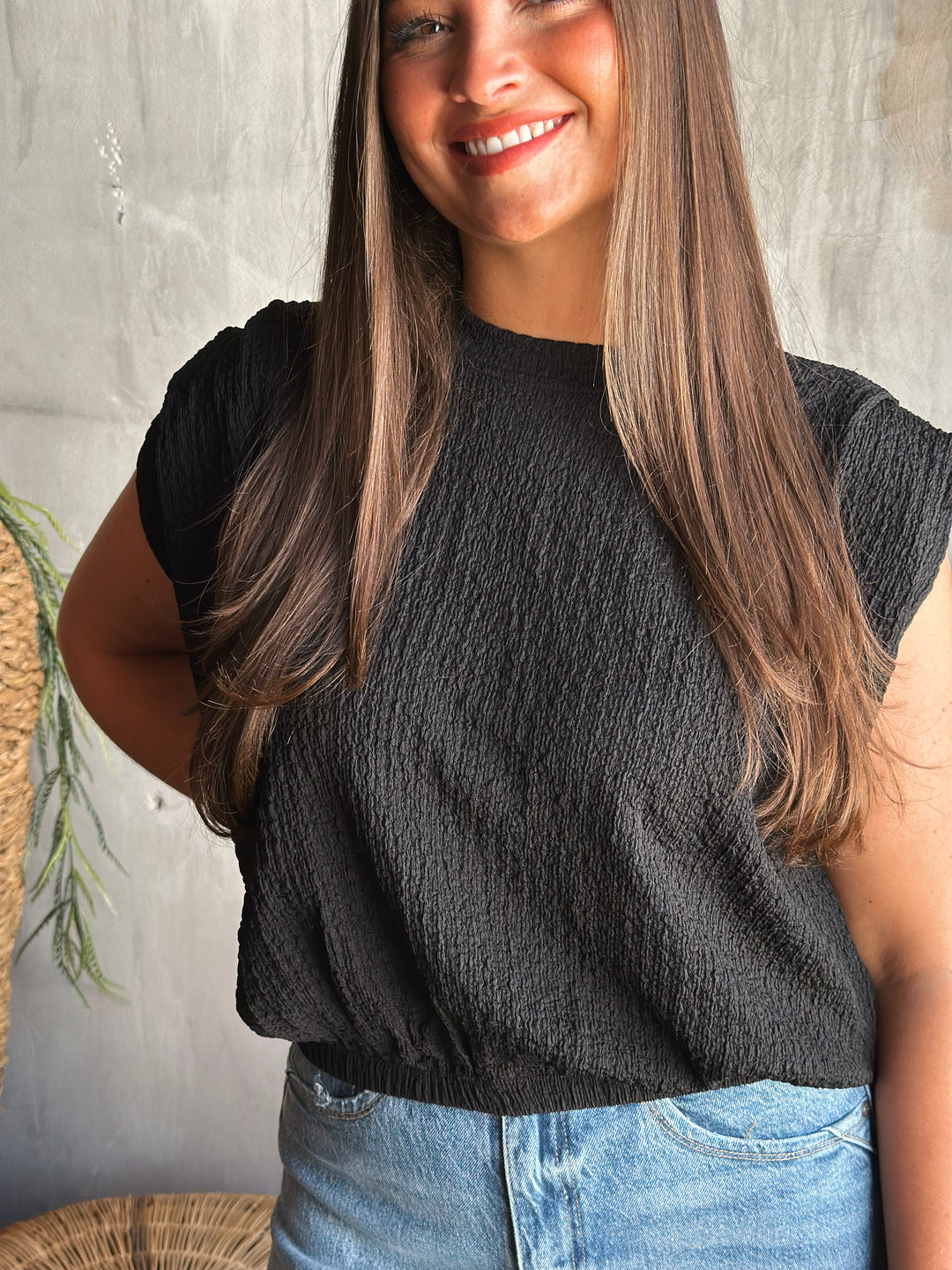 Woman wearing a black textured top and blue jeans against a neutral background