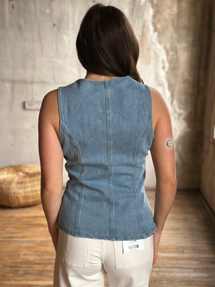 Person wearing a denim sleeveless top with a neutral background