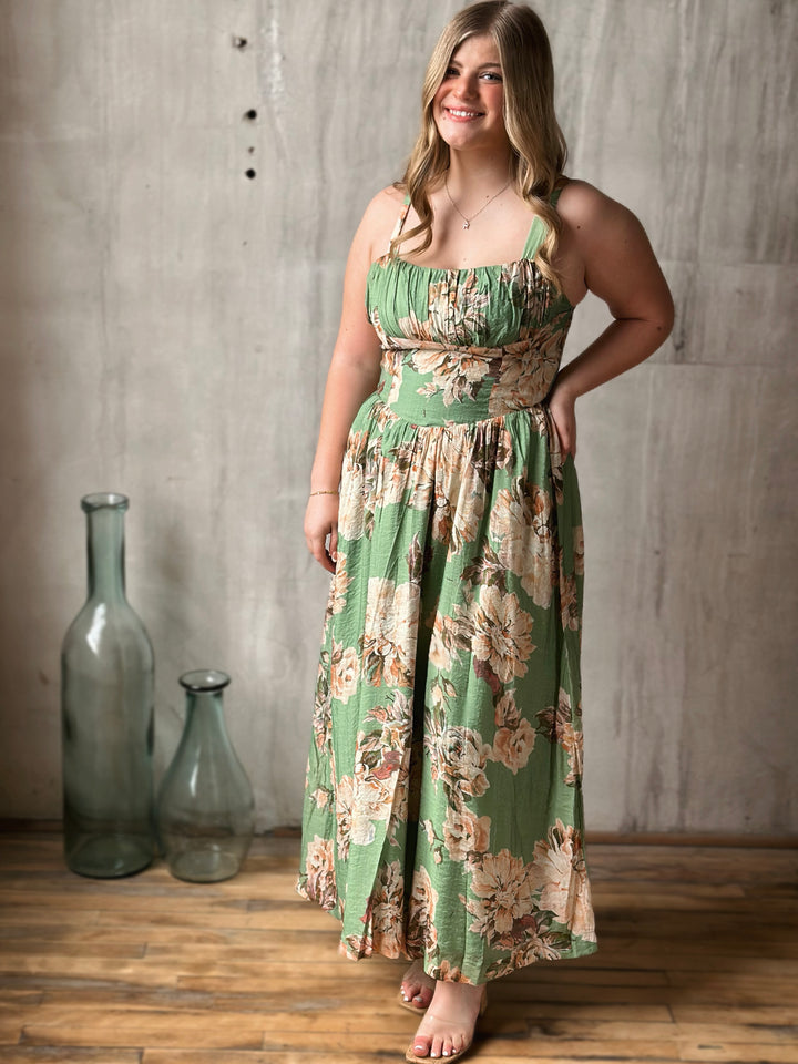 Woman wearing a floral dress standing in a room with wooden floor and gray walls.