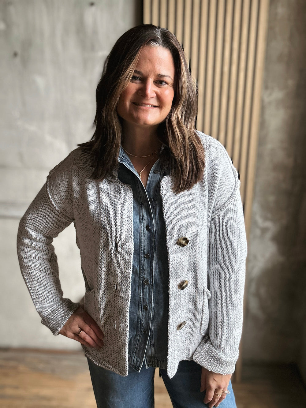 Woman wearing a light gray cardigan over a denim shirt in an indoor setting.