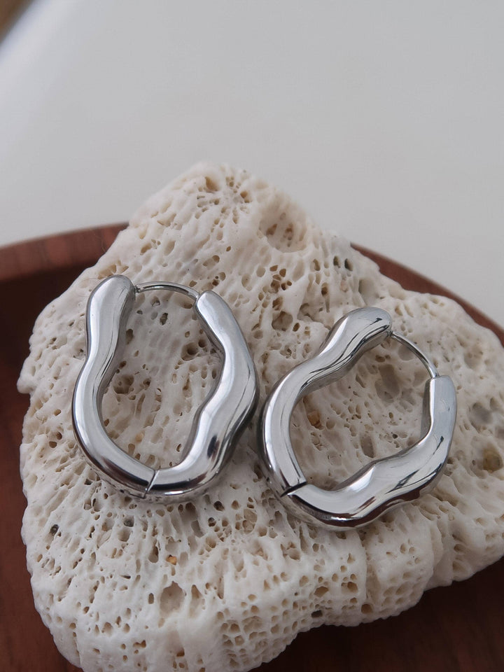 Silver hoop earrings on a textured stone surface