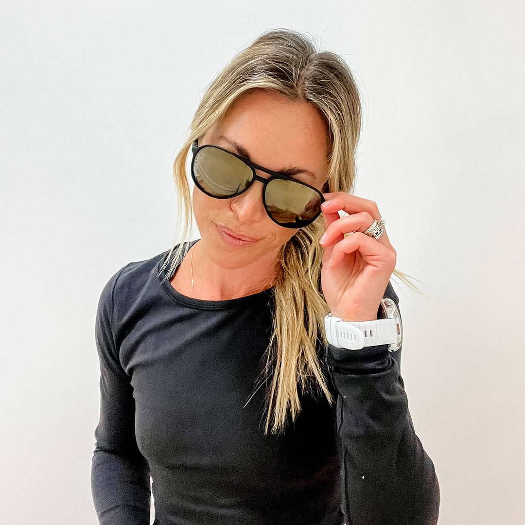 Woman wearing sunglasses and a black long-sleeve shirt against a white background