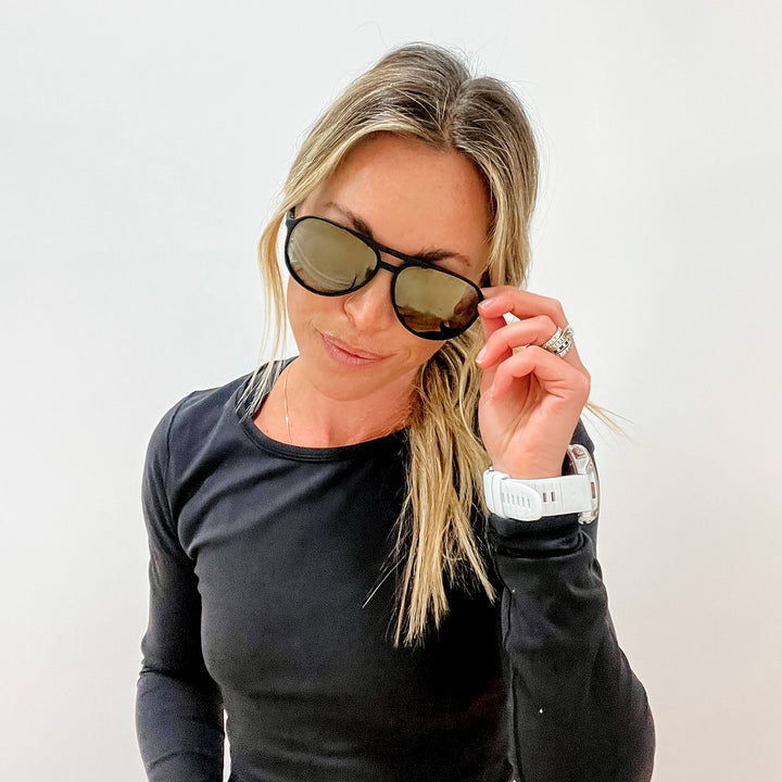 Woman wearing sunglasses and a black long-sleeve shirt against a white background