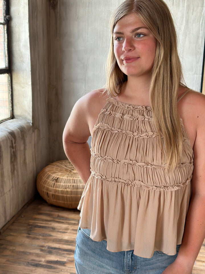 Woman wearing a beige top and blue jeans standing in a room with wooden floor and textured walls.