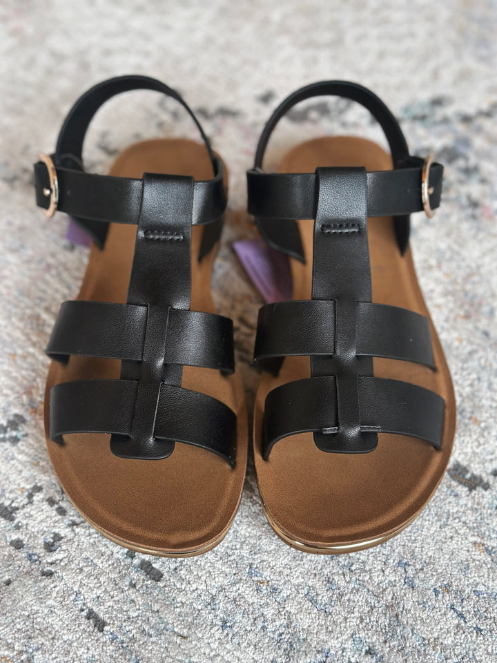 Pair of black strappy sandals on a textured surface.