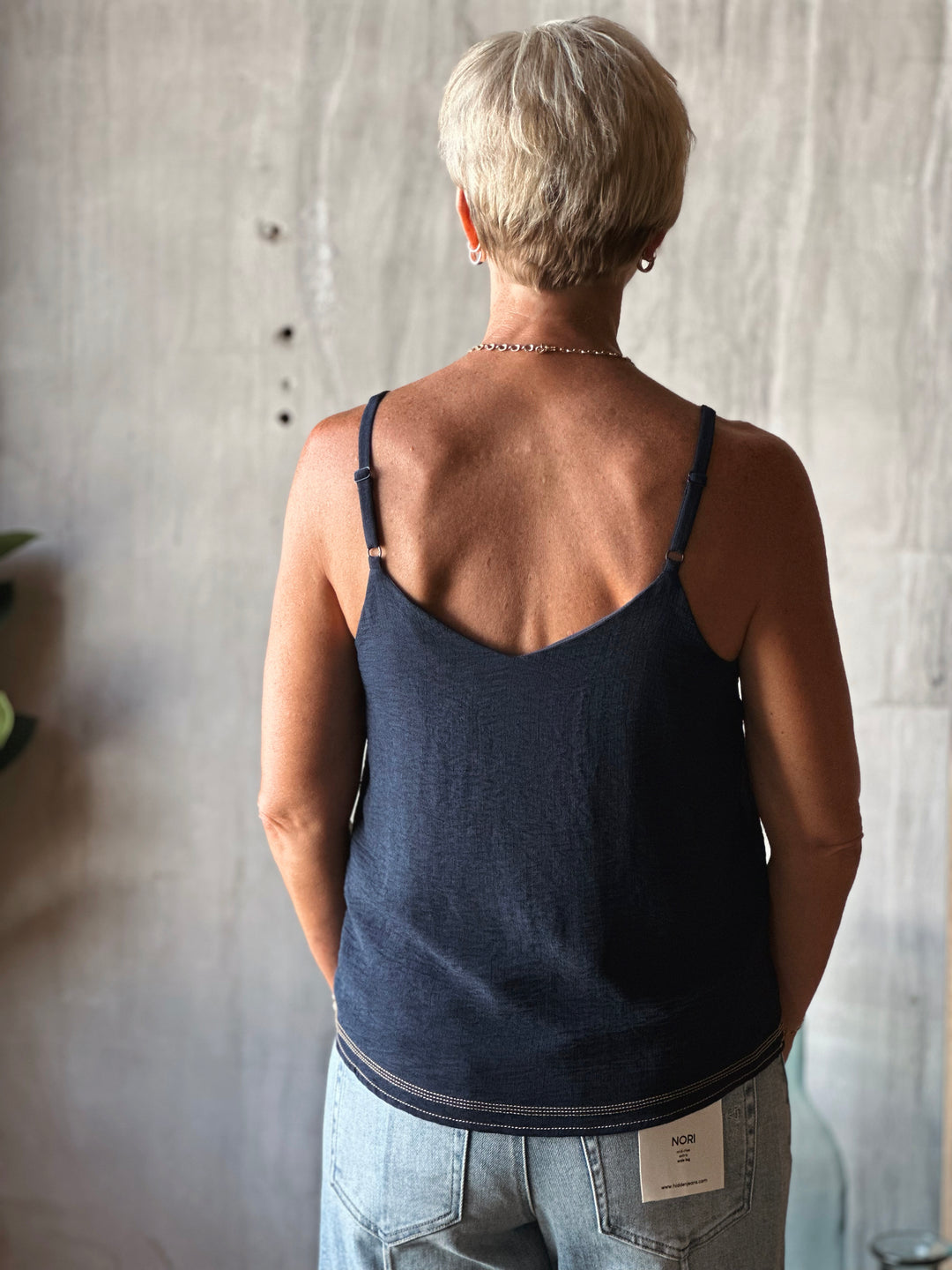 Person wearing a dark blue tank top with a visible brand tag, standing against a neutral wall.