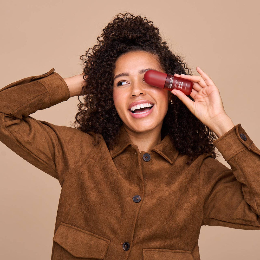 Woman in brown jacket holding a red lipstick against a beige background