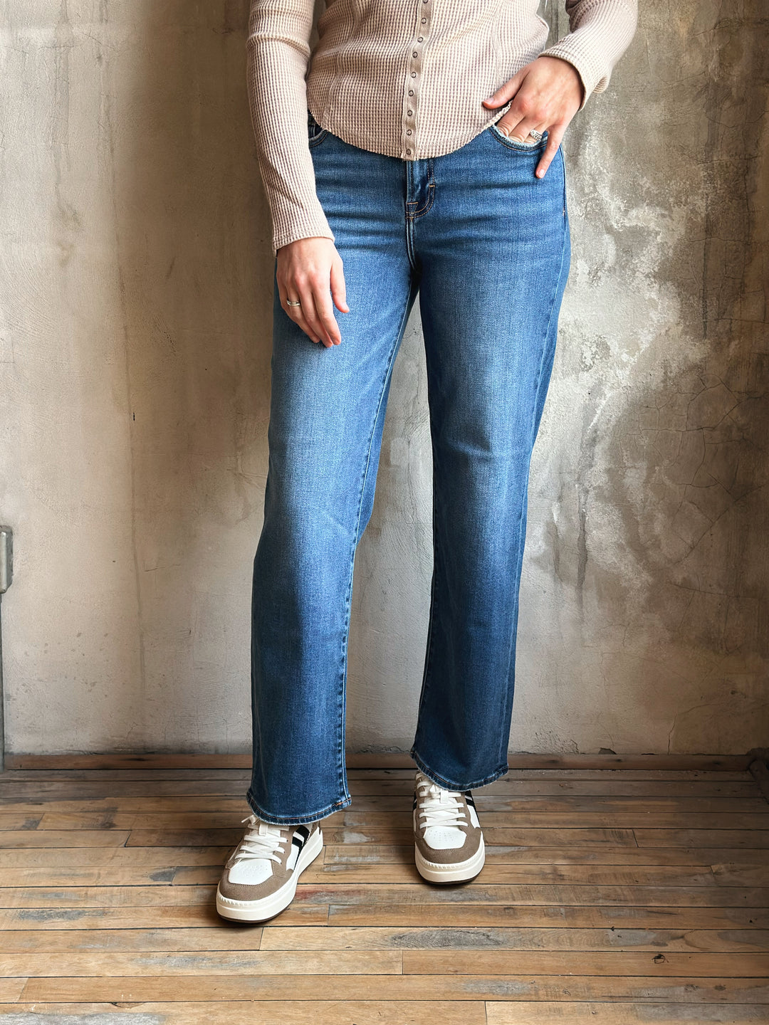 Person wearing blue jeans and a beige shirt against a textured wall.