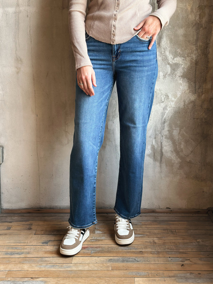 Person wearing blue jeans and a beige shirt against a textured wall.