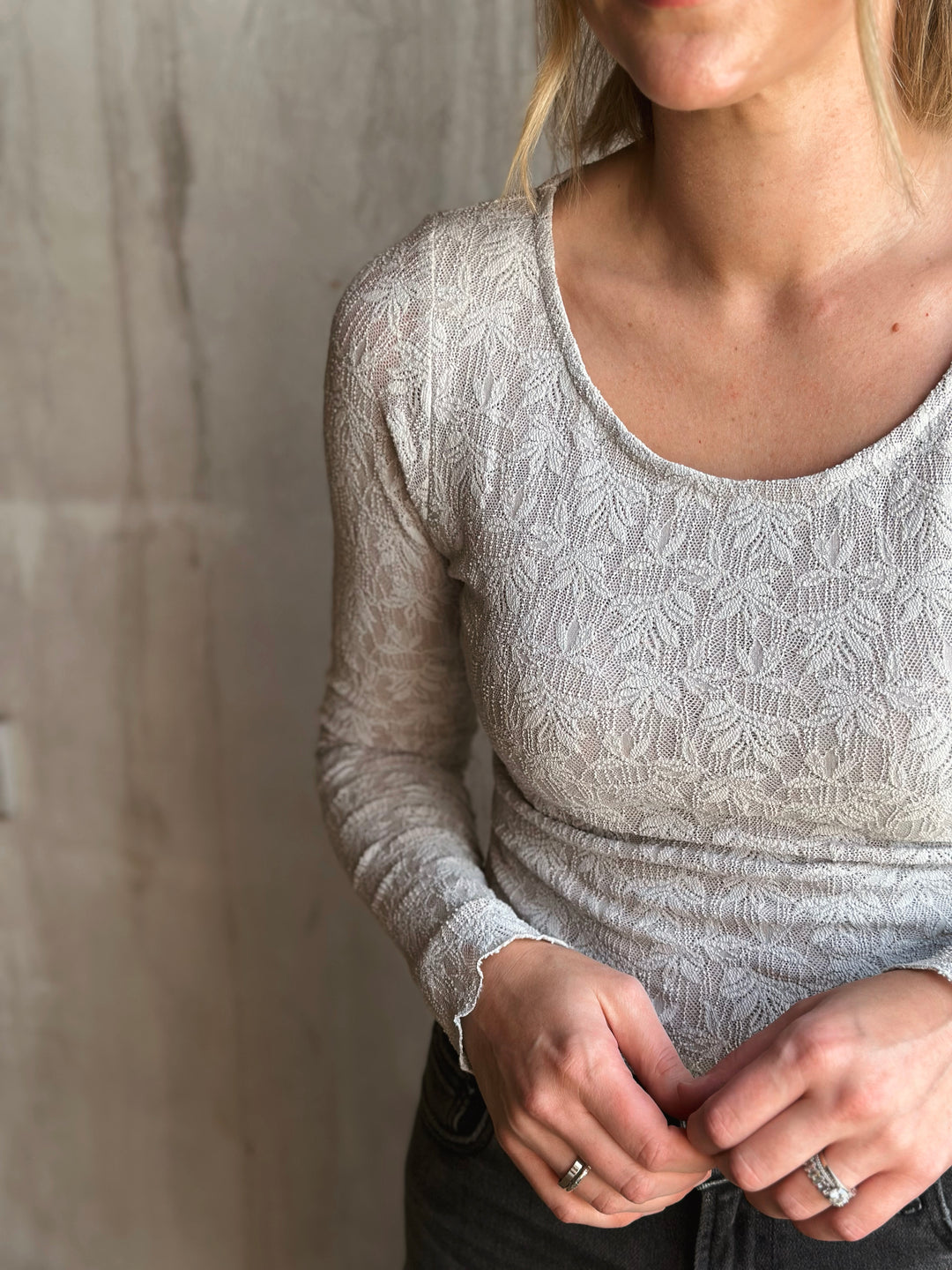 Person wearing a light gray lace top against a neutral background