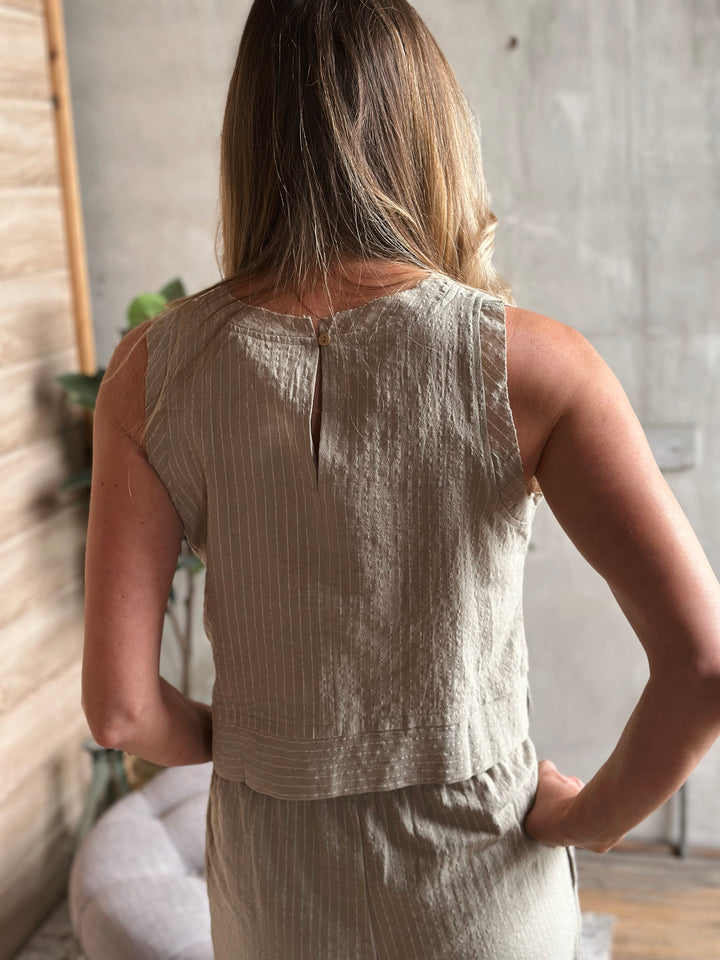Woman wearing a sage sleeveless top and matching pants in a room with a concrete wall.