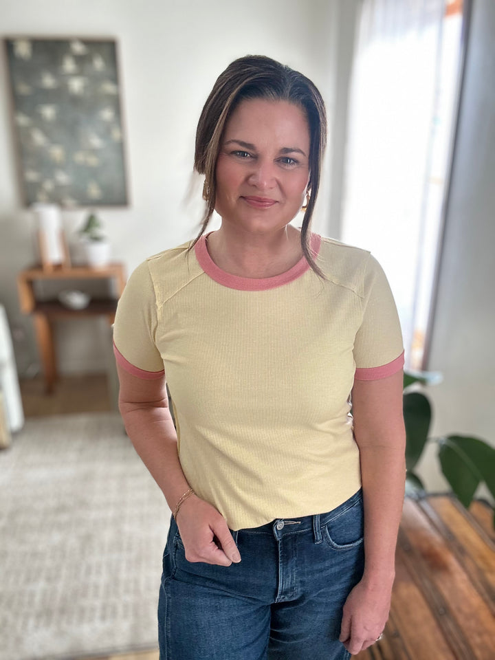 Woman wearing a yellow and pink shirt with blue jeans indoors.