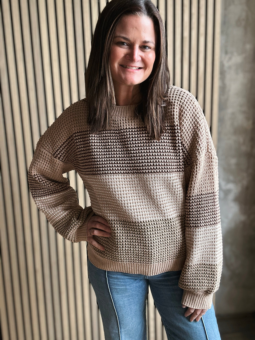 Woman wearing a beige sweater standing against a textured wall.