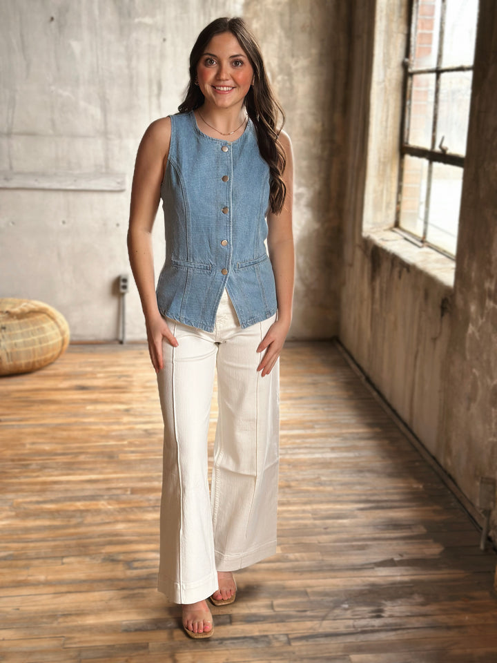 Woman wearing a denim vest with buttons  and white pants in a rustic indoor setting