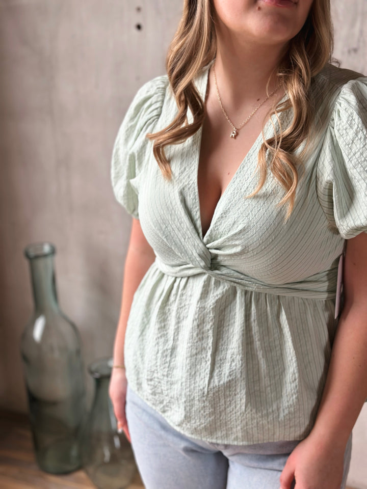 Woman wearing a light green blouse with puffed sleeves against a neutral background