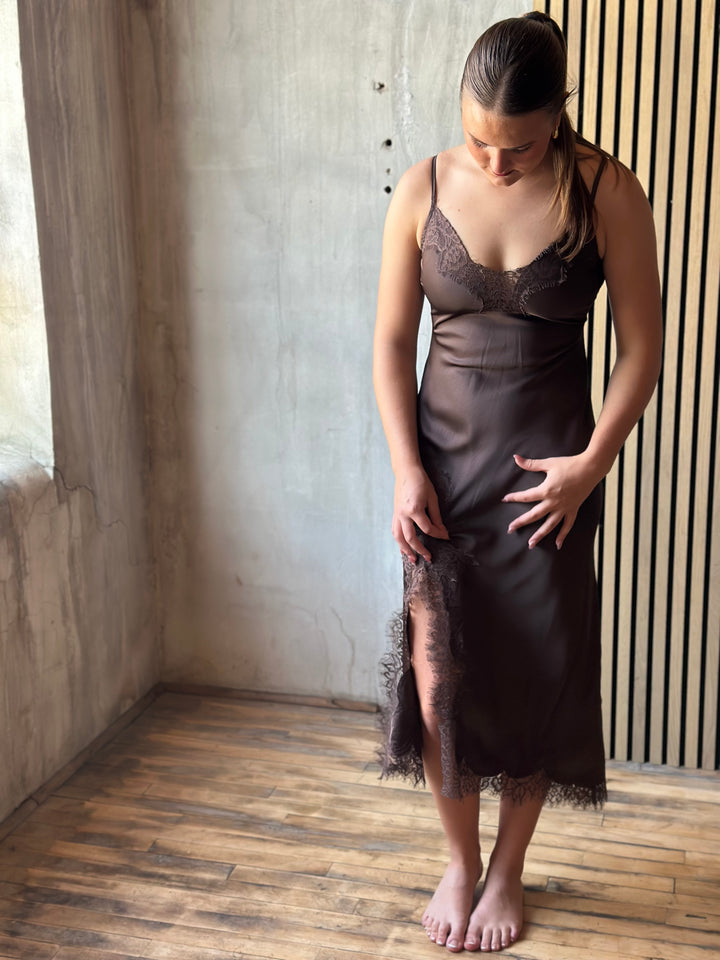 Woman wearing a chocolate brown satin slip dress, looking down at the lace-trimmed slit