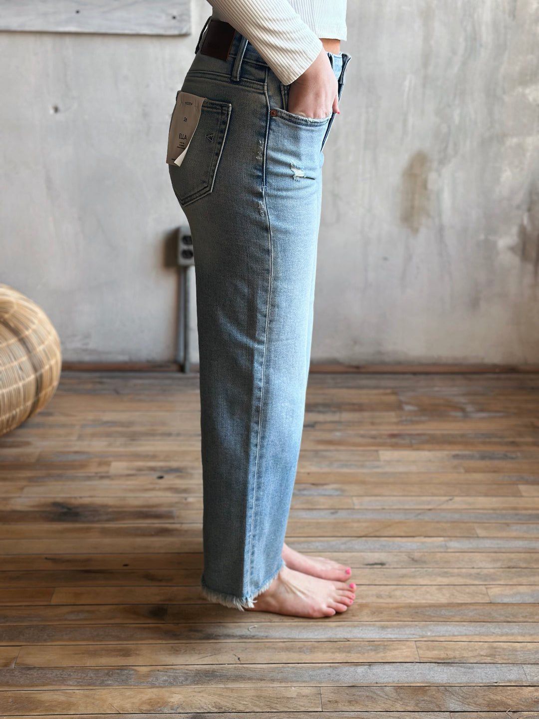 Person wearing light blue jeans standing on a wooden floor with a neutral wall background